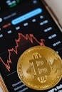 Gold Bitcoin coin on a smartphone showing financial graph, symbolizing digital currency and blockchain trends.